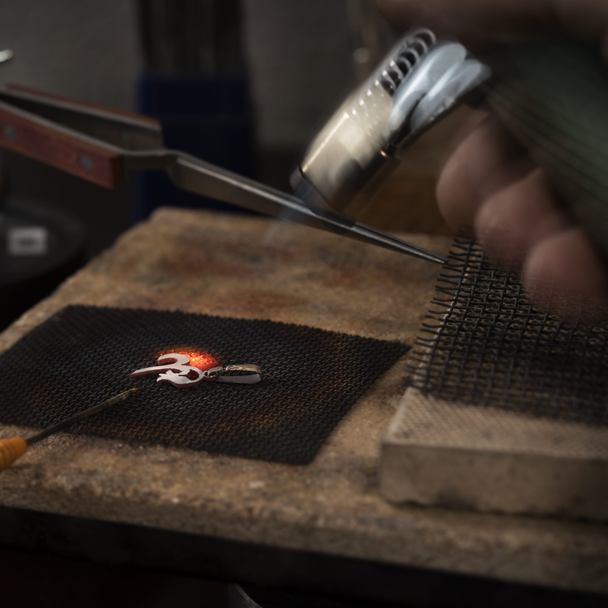 Goldsmith holding a torch soldering a piece of silver on a soldering board or soldering block